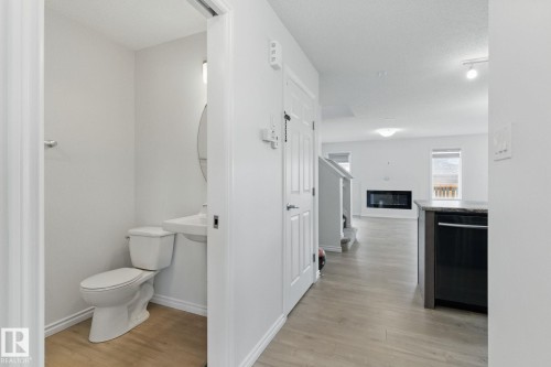 The property features a powder room with a white toilet and pedestal sink, complemented by a round mirror - 2416 Wonnacott Crest, Edmonton, AB - Indoor Photo Showing Bathroom