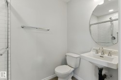 Bathroom featuring a shower with white subway tile, a toilet, and a pedestal sink with a round mirror - 