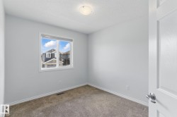 This room features neutral-toned walls, a window with a view of other properties and blue sky, and carpeted flooring - 
