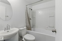 Bathroom featuring a pedestal sink with a chrome faucet, a round wall mirror, and a bathtub with a shower and a patterned shower curtain - 
