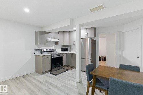 Kitchen featuring light-toned flooring, grey cabinetry, stainless steel appliances, and a dining area with a wooden table - 2416 Wonnacott Crest, Edmonton, AB - Indoor Photo Showing Kitchen