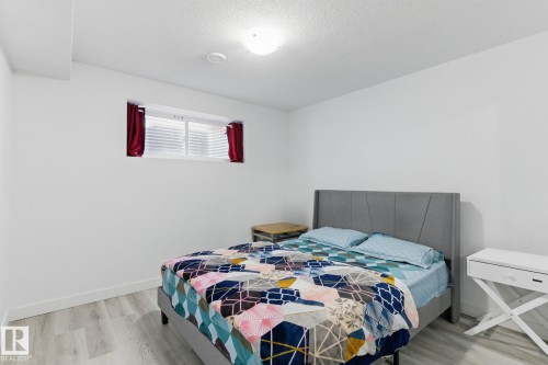 This room features light-colored flooring, a window with horizontal blinds and red curtains, and white walls - 2416 Wonnacott Crest, Edmonton, AB - Indoor Photo Showing Bedroom