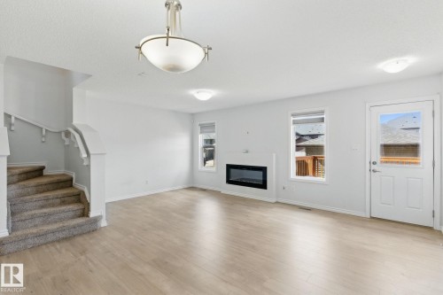This inviting living area features light-colored flooring, a modern fireplace, and large windows that provide natural illumination - 2416 Wonnacott Crest, Edmonton, AB - Indoor Photo Showing Living Room With Fireplace