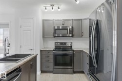 The kitchen features stainless steel appliances, grey cabinetry, light countertops, and a double basin sink with a chrome faucet - 
