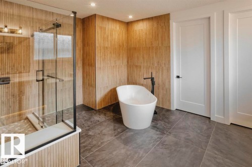 Luxurious bathroom featuring a freestanding white bathtub, a glass-enclosed shower, and walls with textured wood-look tiling - 63 Jubilation Drive, St. Albert, AB - Indoor Photo Showing Bathroom