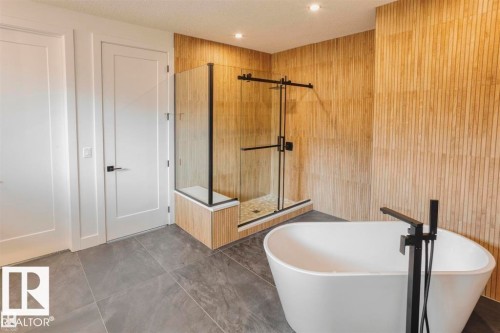 The bathroom features a freestanding bathtub with a matte black floor-mounted faucet, a glass-enclosed shower with black hardware, and wood-paneled walls - 63 Jubilation Drive, St. Albert, AB - Indoor Photo Showing Bathroom