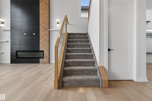 Modern staircase featuring carpeted treads with integrated lighting, a light wood-finish handrail, and clear panel balusters - 63 Jubilation Drive, St. Albert, AB - Indoor Photo Showing Other Room