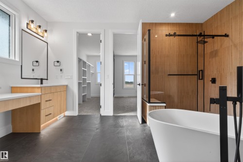 Modern bathroom featuring a freestanding tub, a large walk-in shower with natural wood-look wall tiling, a vanity with a white countertop and wood-finish cabinetry, and dark tile flooring - 63 Jubilation Drive, St. Albert, AB - Indoor