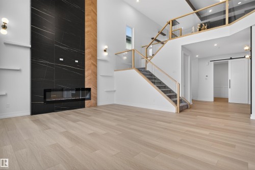 Two-story living area featuring a prominent black tiled fireplace with an integrated linear electric fireplace, wood-finish flooring, and a contemporary staircase with glass railings - 63 Jubilation Drive, St. Albert, AB - Indoor With Fireplace