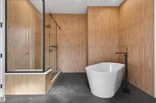 Freestanding soaking tub with a matte black floor-mounted faucet, complemented by a spacious glass-enclosed shower featuring a rain showerhead - 63 Jubilation Drive, St. Albert, AB - Indoor Photo Showing Bathroom
