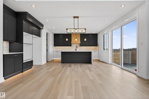 Modern kitchen featuring dark cabinetry, a light wood-finish floor, and a central island - 63 Jubilation Drive, St. Albert, AB - Indoor Photo Showing Kitchen
