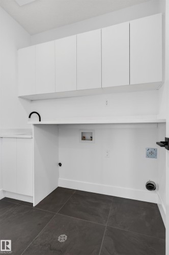 Dedicated utility space featuring white cabinetry, a built-in countertop, dark tile flooring, and essential appliance hookups - 63 Jubilation Drive, St. Albert, AB - Indoor