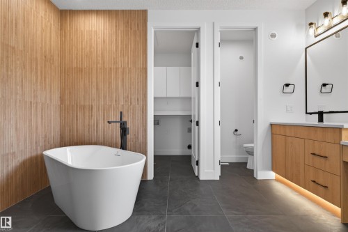 Freestanding tub with a matte black floor-mounted faucet, set against a textured wood-finish accent wall - 63 Jubilation Drive, St. Albert, AB - Indoor Photo Showing Bathroom