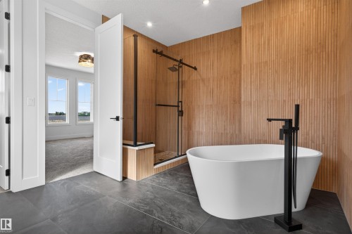 Contemporary bathroom featuring a freestanding soaking tub with matte black floor-mounted faucet, a glass-enclosed shower with a sliding barn door, and fluted wood-finish accent walls - 63 Jubilation Drive, St. Albert, AB - Indoor Photo Showing Other Room