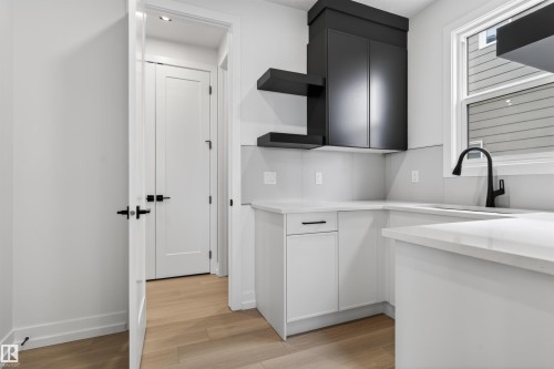Modern kitchen area featuring white cabinetry, light countertops, black upper cabinets, and a black gooseneck faucet - 63 Jubilation Drive, St. Albert, AB - Indoor Photo Showing Kitchen