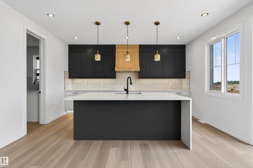 Modern kitchen featuring a large central island with a waterfall countertop, dark cabinetry, wood-finish flooring, and recessed lighting - 63 Jubilation Drive, St. Albert, AB - Indoor Photo Showing Kitchen