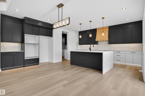 Open-concept kitchen featuring two-tone cabinetry, a large center island with a waterfall countertop, wood-finish flooring, recessed lighting, and a linear pendant light fixture - 63 Jubilation Drive, St. Albert, AB - Indoor Photo Showing Kitchen With Upgraded Kitchen