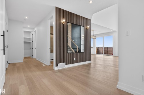 Spacious interior featuring wide plank wood-finish flooring, a contemporary slat accent wall with sconce lighting, an open-concept living area with high ceilings, large sliding glass doors, and recessed lighting throughout - 63 Jubilation Drive, St. Albert, AB - Indoor Photo Showing Other Room
