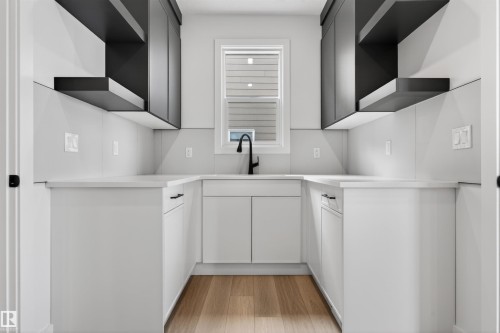 Modern kitchen featuring light wood-finish flooring, white lower cabinetry with dark hardware, and contrasting dark upper cabinetry with open shelving - 63 Jubilation Drive, St. Albert, AB - Indoor Photo Showing Kitchen