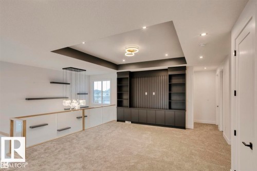 This spacious area features a tray ceiling with recessed lighting, a modern chandelier, and a built-in media console with shelving - 63 Jubilation Drive, St. Albert, AB - Indoor Photo Showing Other Room