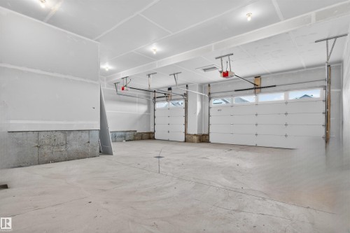 Spacious garage featuring two overhead doors with window accents, concrete flooring, and unfinished drywall walls - 63 Jubilation Drive, St. Albert, AB - Indoor Photo Showing Garage
