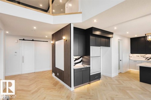 The property features chevron-patterned light wood flooring, recessed lighting, and a modern kitchen with dark cabinetry and light countertops - 63 Jubilation Drive, St. Albert, AB - Indoor Photo Showing Kitchen