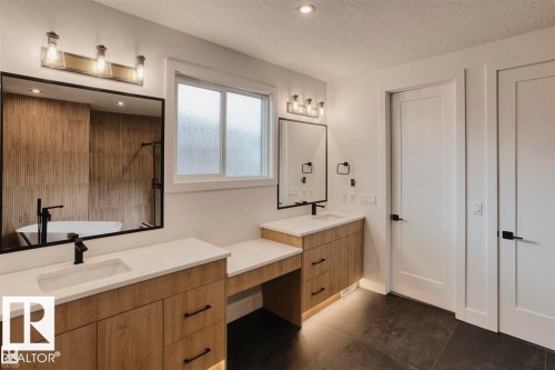 This bathroom features dual vanities with light wood cabinetry, white countertops, and black fixtures - 63 Jubilation Drive, St. Albert, AB - Indoor