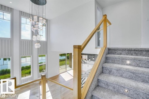 The property features a grand entry with a multi-story wall of windows, a contemporary chandelier, and a carpeted staircase with integrated lighting - 47 Rosewood Way, St. Albert, AB - Indoor Photo Showing Other Room
