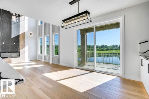 Spacious interior featuring light hardwood flooring, a modern linear fireplace with a dark stone surround, and large windows providing views of the waterfront - 47 Rosewood Way, St. Albert, AB -  With Exterior