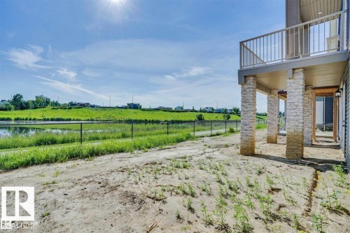 The property features a balcony with metal railings and stone-clad pillars, overlooking a body of water and a grassy landscape - 47 Rosewood Way, St. Albert, AB - Outdoor With Balcony