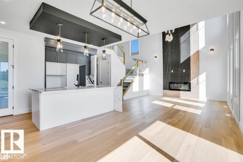 This bright open concept living area features light hardwood flooring, a modern fireplace with a dark stone surround, and high ceilings - 47 Rosewood Way, St. Albert, AB - Indoor
