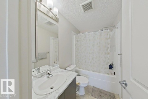 The bathroom features a vanity with a white countertop and an integrated sink, illuminated by an overhead light fixture - 429 390 Windermere Rd, Edmonton, AB - Indoor Photo Showing Bathroom