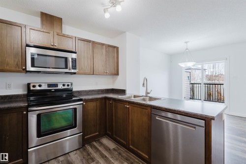 Kitchen with stainless steel appliances, a peninsula, dark wood-style floors, a textured ceiling, and decorative light fixtures - Edmonton, AB - Indoor Photo Showing Kitchen With Stainless Steel Kitchen With Double Sink