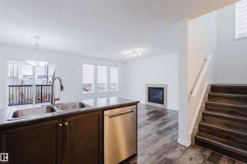 Kitchen featuring dishwasher, a tiled fireplace, dark wood finish cabinets, dark wood finished floors, and hanging light fixtures - Edmonton, AB - Indoor Photo Showing Kitchen With Double Sink