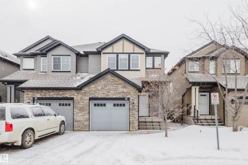 Craftsman-style house featuring stone siding, an attached garage, and roof with shingles - Edmonton, AB - Outdoor With Facade
