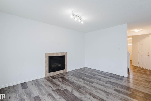 Unfurnished living room with a tiled fireplace and wood finished floors - Edmonton, AB - Indoor Photo Showing Living Room With Fireplace