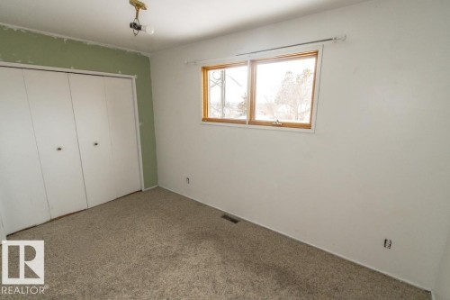 This room features a window with wood trim, a carpeted floor, and a closet with bifold doors - 5016 47 St, Myrnam, AB - Indoor Photo Showing Other Room