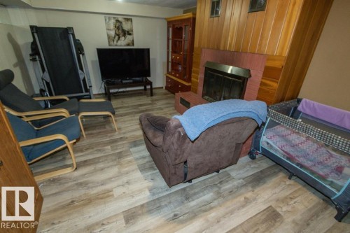This room features wood-look flooring, a fireplace with a brick surround, and wood paneling - 5016 47 St, Myrnam, AB - Indoor With Fireplace