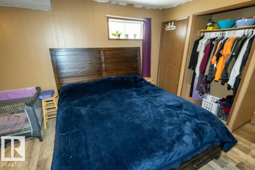 The bedroom features a wooden headboard, a window with natural light, and an open closet with shelving - 5016 47 St, Myrnam, AB - Indoor Photo Showing Bedroom