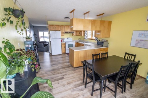 The kitchen features wood cabinetry, white appliances, and light countertops, with a dining area providing space for gatherings - 5016 47 St, Myrnam, AB - Indoor