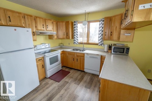 Kitchen featuring wood cabinetry, white appliances, and a window above the sink - 5016 47 St, Myrnam, AB - Indoor Photo Showing Kitchen With Double Sink