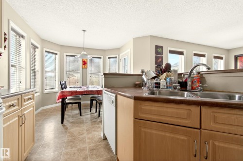 The kitchen features light-toned cabinetry, a stainless steel double sink, and a dishwasher, with tiled flooring throughout - 8922 5 Avenue, Edmonton, AB - Indoor Photo Showing Kitchen With Double Sink