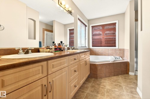The bathroom features a double vanity with light wood cabinetry, a built-in corner bathtub, and tiled flooring - 8922 5 Avenue, Edmonton, AB - Indoor Photo Showing Bathroom