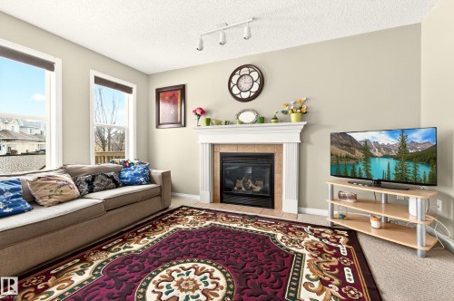 The living area features a fireplace with a mantel, track lighting, and two large windows - 8922 5 Avenue, Edmonton, AB - Indoor Photo Showing Living Room With Fireplace
