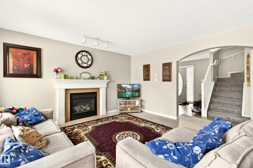 The living area features a white fireplace with a mantel, track lighting, and a carpeted floor - 8922 5 Avenue, Edmonton, AB - Indoor Photo Showing Living Room With Fireplace
