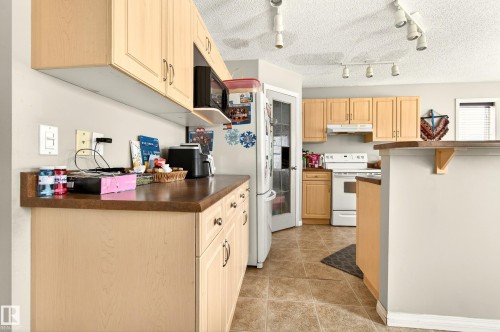 The kitchen features wood cabinetry, a built-in microwave, and track lighting - 8922 5 Avenue, Edmonton, AB - Indoor Photo Showing Kitchen