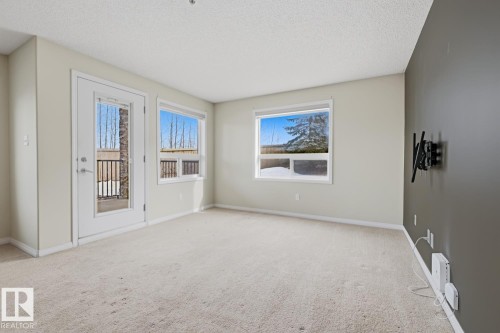This living space features a light-colored carpet, white walls, and a dedicated accent wall - 125 1520 Hammond Gate Nw, Edmonton, AB - Indoor Photo Showing Other Room