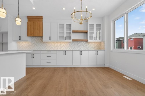 The kitchen features light-toned cabinetry with dark hardware, a herringbone pattern backsplash, and a wooden range hood - 5 Rosa Crescent, St. Albert, AB - Indoor Photo Showing Kitchen
