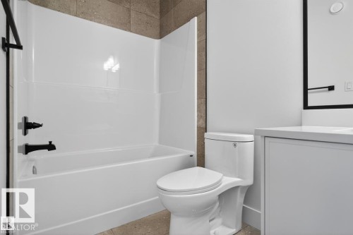 Bathroom featuring a white bathtub with dark fixtures, a toilet, a vanity with a white countertop, and a mirror with a dark frame - 5 Rosa Crescent, St. Albert, AB - Indoor Photo Showing Bathroom