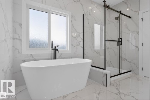 The bathroom features a freestanding soaking tub with a modern black floor-mounted faucet, a glass-enclosed shower with black framing, and white marble-look tile flooring and walls - 5 Rosa Crescent, St. Albert, AB - Indoor Photo Showing Bathroom